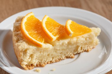 Portakallarla süslenmiş bir tabakta bir dilim cheesecake.