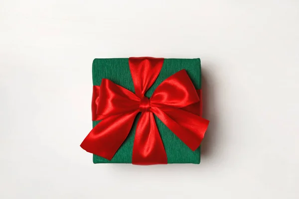 Close-up de uma caixa verde com um presente e uma fita vermelha em um fundo branco — Fotografia de Stock