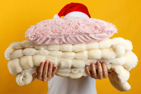 Mujer en sombrero de santa sosteniendo una pila de cálidos cuadros esponjosos y almohadas sobre un fondo de una pared amarilla — Foto de Stock