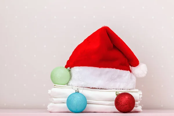 Temiz bir yatak yığını ve Noel Baba şapkası. Arka planda bir masanın üstünde Noel topları.