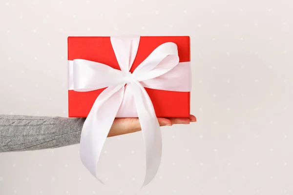 Κλείσιμο κουτιού με δώρο και φιόγκο σε γυναικείο χέρι σε ανοιχτόχρωμο φόντο τοίχου — Φωτογραφία Αρχείου