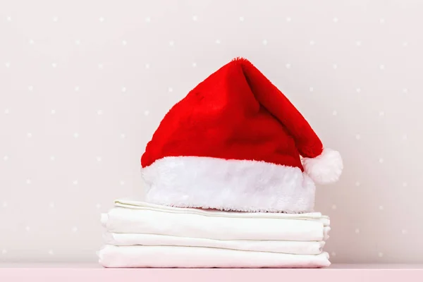 Bir yığın temiz beyaz yatak ve bir Noel Baba şapkası, bir masanın üzerinde, ışık duvarına karşı. Boşluğu kopyala
