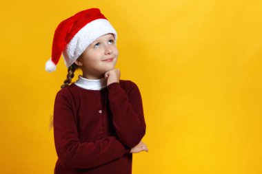 Sarı arka planda Noel Baba şapkalı sevimli bir bebek. Küçük kız rüya görüyor.