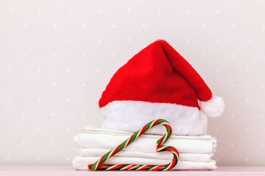 Temiz beyaz bir yatak yığını, Noel Baba şapkası ve Noel şekeri, bir ışık duvarının arka planında. Boşluğu kopyala