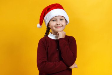 Noel ve Yeni Yıl konsepti. Sarı arka planda Noel Baba şapkalı sevimli bir çocuk. Küçük kız gülümser ve hayal kurar