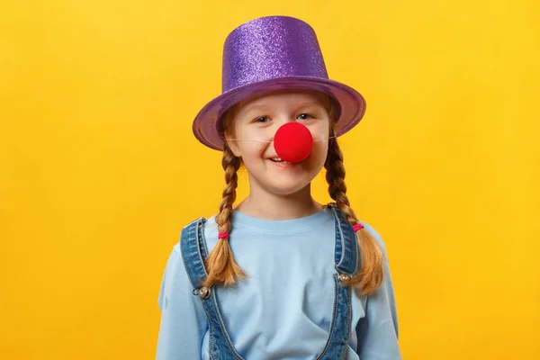Clown bambino divertente, cappello e un naso rosso. Ragazzina allegra su sfondo giallo. 1 aprile. April Fools Day. Copia spazio — Foto Stock