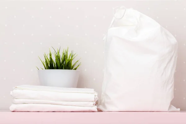 Gros plan d'une pile de literie blanche, sac de rangement, plante d'intérieur sur une table sur le fond d'un mur léger — Photo