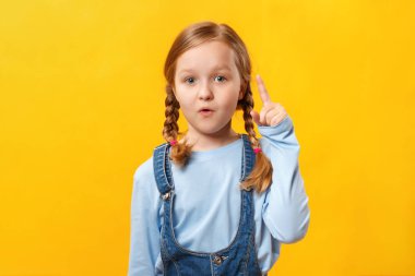 Küçük kız işaret parmağıyla boş bir yerde beliriyor. Sarı arka plandaki çocuk. Boşluğu kopyala