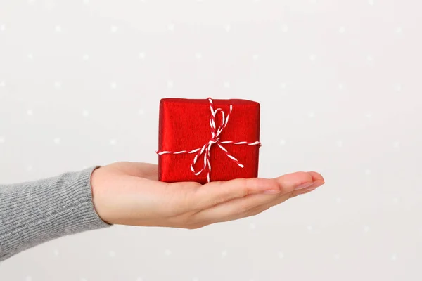 Primer plano de una pequeña caja roja con un regalo en una mano femenina, sobre un fondo de pared claro — Foto de Stock