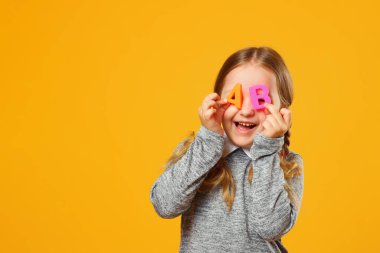 Sarı arka planda neşeli küçük bir kızın portresi. Liseli kızda A ve B harfleri var. Eğitim ve okul kavramı