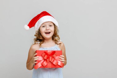 Gri arka planda mutlu, gülümseyen sarışın bir kızın portresi. Noel Baba şapkalı bir çocuk elinde hediyeli kırmızı bir kabuk tutuyor. Noel kutlaması kavramı