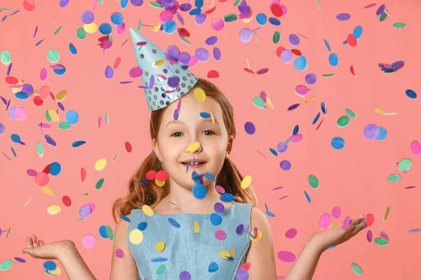 Cheerful little girl celebrates birthday. A child is standing in a rain of confetti. A party. Closeup portrait on pink background — Stock Photo, Image