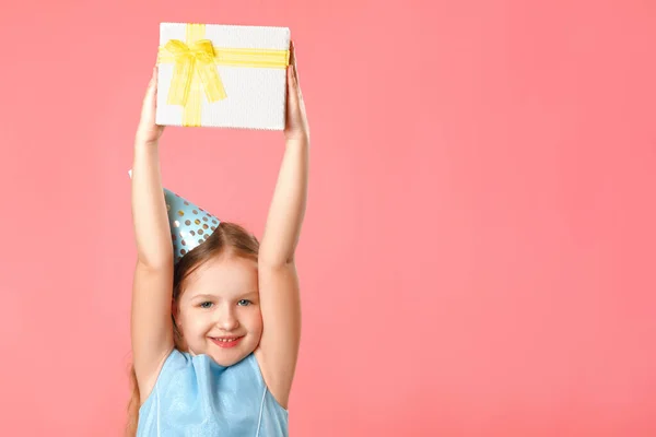 A happy little girl in a cap holds a box with a gift above her head. Portrait of a child on a pink coral background. Copy space — Stock Photo, Image
