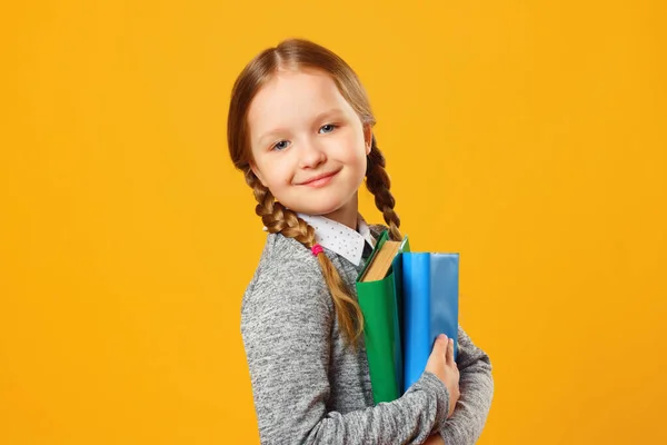 Primo piano ritratto di bambina scolara su sfondo giallo. Il bambino ha dei libri di testo. Il concetto di istruzione e scuola — Foto Stock