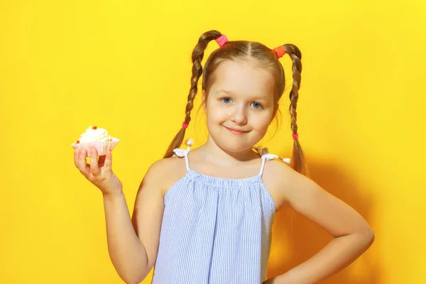 Detailní portrét veselé holčičky na žlutém pozadí. Dítě s copánky ve vlasech, držící v rukou dort — Stock fotografie