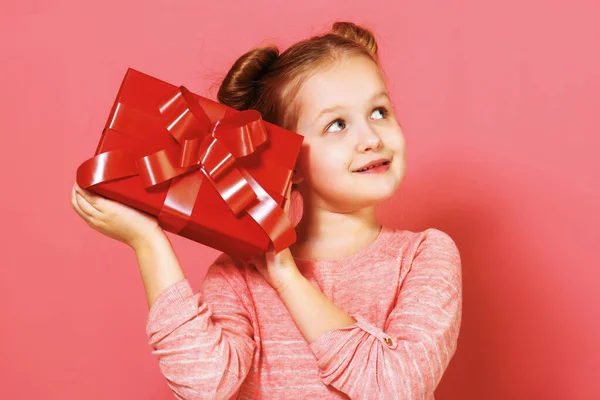 Ritratto ravvicinato di una bambina con ciuffi di capelli su sfondo rosa. Un bambino tiene una scatola con un regalo in mano, pensa, fantastica, sogna — Foto Stock