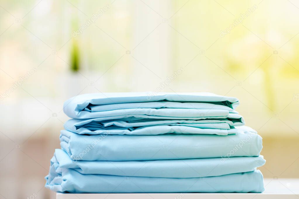 Close-up of blue clean bedding on a blurred background. A stack of folded new bed sheets on the table. Sunlight from the window