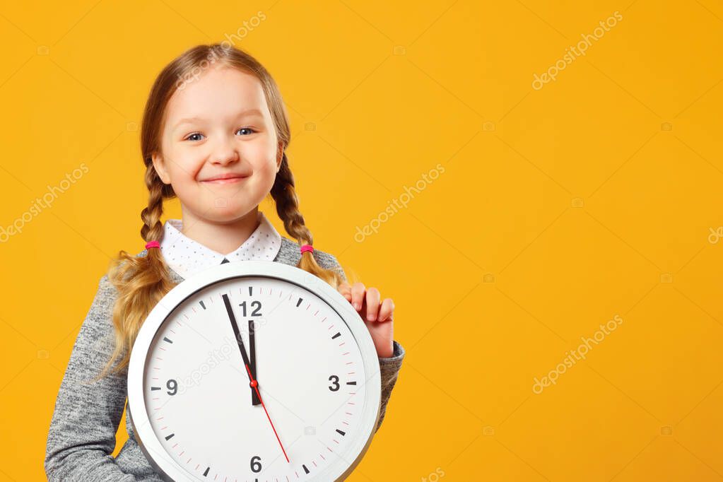 Little girl holding a big clock on a yellow background. The concept of education, school, deadline, time to learn