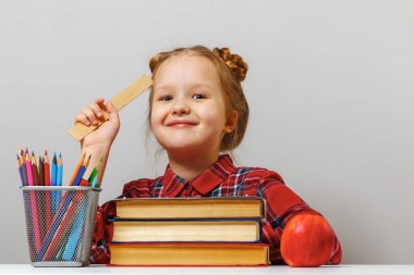 Gözlüklü sevimli küçük bir kız elinde cetvelle masada oturuyor. Liseli kız kitaplar ve kalemlerle çevrilidir. Eğitim kavramı