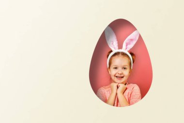 Tavşan kulaklı şirin bir kız bebek. Renkli pembe ve beyaz bir arka planda yumurta şeklinde bir çocuk. Paskalya konsepti