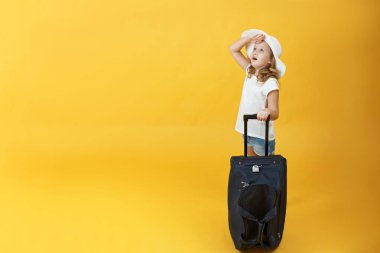 Küçük bir sarışın çocuk kız seyahat etmeye hazır, bir bavul ile duruyor ve gökyüzüne bakar. Sarı arka plan