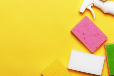 Deterjanlı sprey şişesi, sarı arka planda sünger. Temizlik kavramı