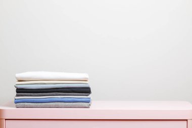 Pembe bir masanın üzerinde katlanmış giysiler var. Gri arka plan. Yakın plan.