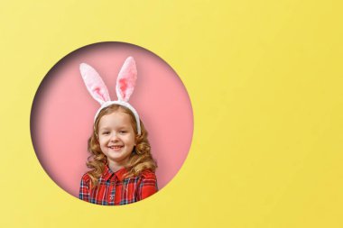 Tavşan kulaklı şirin bir kızın portresi. Mutlu Paskalyalar. Renkli pembe ve sarı arka planda yuvarlak bir çember içindeki çocuk