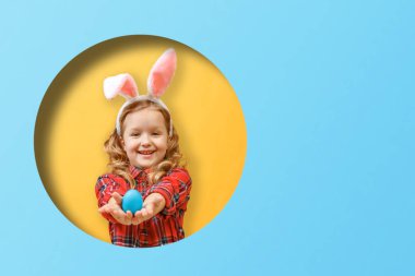 Paskalya yumurtalı tavşan kulaklı neşeli küçük kız. Renkli sarı ve mavi arka planda yuvarlak bir çember içindeki çocuk