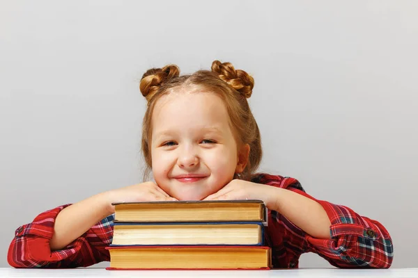 Ragazzina carina seduta a tavola, appoggiata a libri spessi. Concetto educativo — Foto Stock