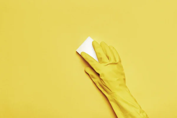 Ręka w gumowej rękawicy ochronnej z białą gąbką na żółtym tle. Koncepcja czyszczenia — Zdjęcie stockowe