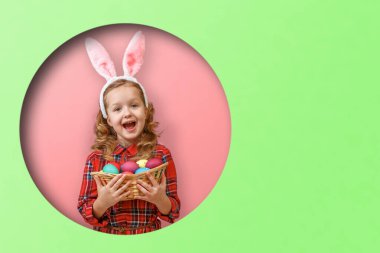 Paskalya yumurtası sepeti tutan tavşan kulaklı şirin bir kız. Renkli yeşil ve pembe arka planda yuvarlak bir çember içindeki çocuk.