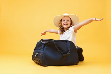Seyahat hayalleri. Küçük bir kız çocuğu bir bavulun içinde oturur ve uçağın pilotunu ve gezgini oynar. Sarı arkaplan