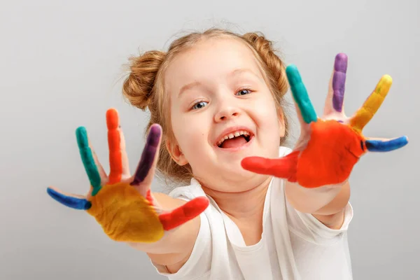 Niño alegre niña muestra las manos pintadas con pintura. Fondo gris, retrato —  Fotos de Stock