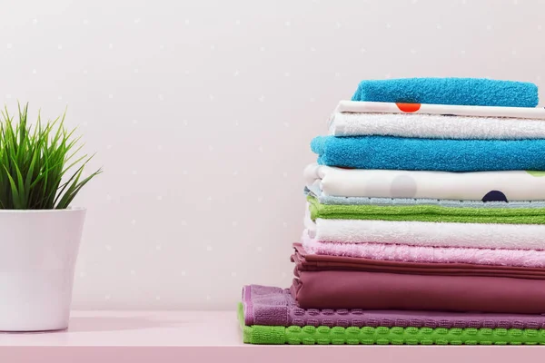 Sur la commode, il y a une pile de linge de lit repassé propre, des serviettes pliées multicolores et une plante à la maison. — Photo
