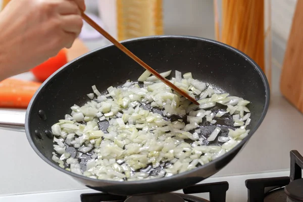 Домашняя кухня. Женщина жарит лук в горячей сковороде с растительным маслом. Крупный план — стоковое фото