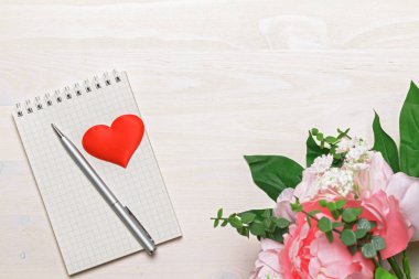 Beyaz ahşap arka planda sarmal, gri kalem, kalp ve pembe şakayık çiçekli boş not defteri. Üst Manzara. Boşluğu kopyala