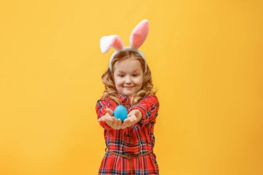 Renkli arka planda paskalya yumurtası olan tavşan kulaklı neşeli küçük kız.