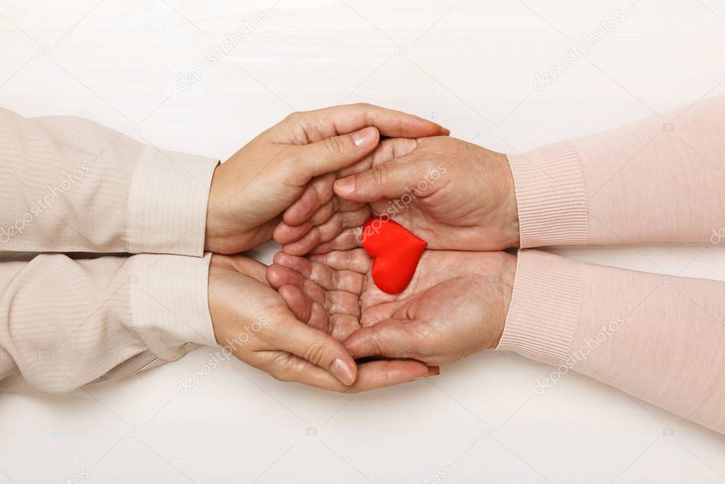 Close-up of the hand of an adult daughter and an older mother holding a heart together. Top view. Family and care concept