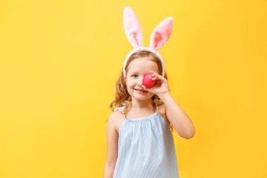 Renkli arka planda paskalya yumurtası olan tavşan kulaklı neşeli küçük kız.