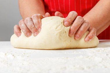 Kıdemli kadın taze hamur yoğurur ve ellerini masaya koyar.