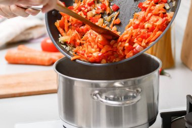 Ev yapımı yemek. Tavadan bir kadın tencereye kızarmış sebze ekliyor. Yakın plan.