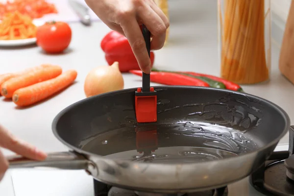 Домашняя кухня. Женщина смазывает сковороду маслом на газовой плите, рядом со свежими овощами и макаронами — стоковое фото