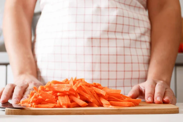 Una mujer cocina en la cocina, sobre una tabla de madera se encuentra un montón de zanahorias picadas. Comida fresca y saludable. Primer plano — Foto de Stock