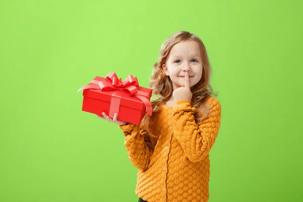 Ritratto di bambina in maglione caldo su sfondo rosa verde ufo. Il bambino guarda sognante e tiene una scatola rossa con un regalo. Il concetto di celebrazione, dare e ricevere un dono — Foto Stock