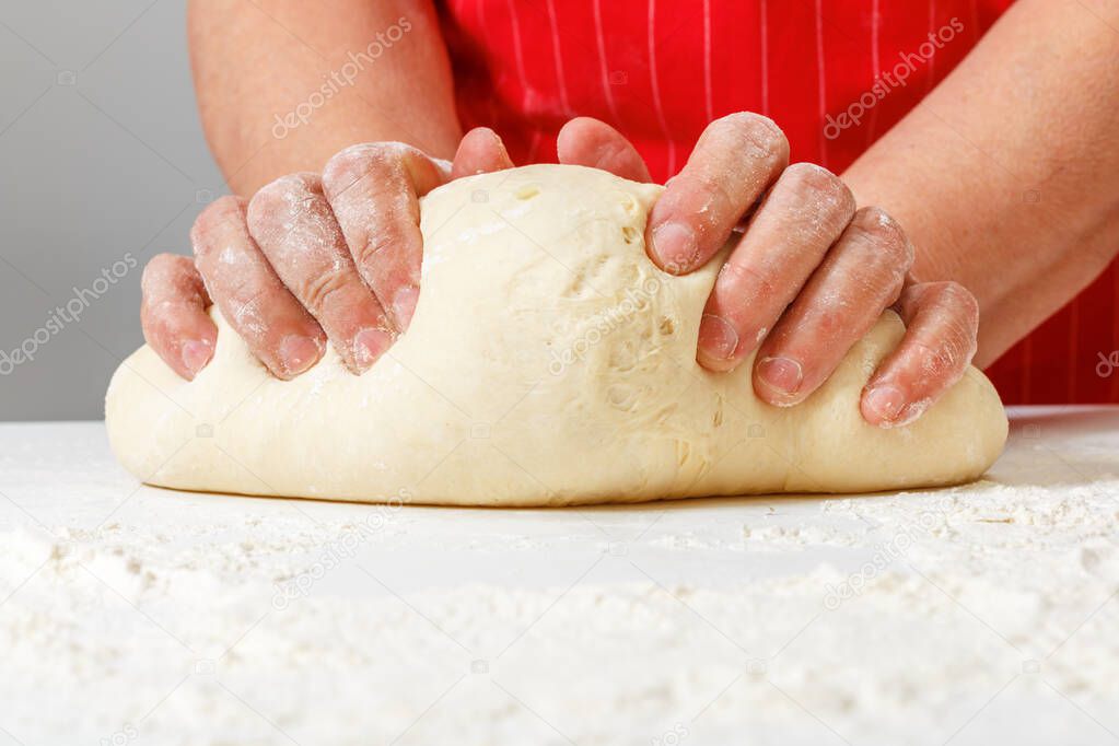 Senior woman kneads raw fresh dough with hands on the table