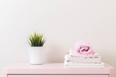 A pile of clean ironed bedding and a towel lies on the dresser