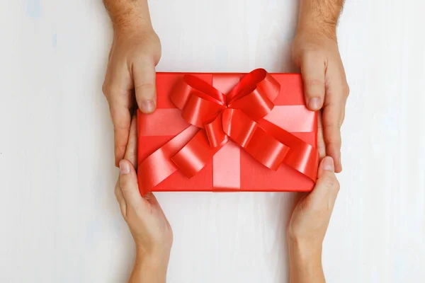 Closeup of a man's hand giving a red box with a gift to a woman. Top view. Concept of Valentine's Day and Christmas celebration — Stock Photo, Image