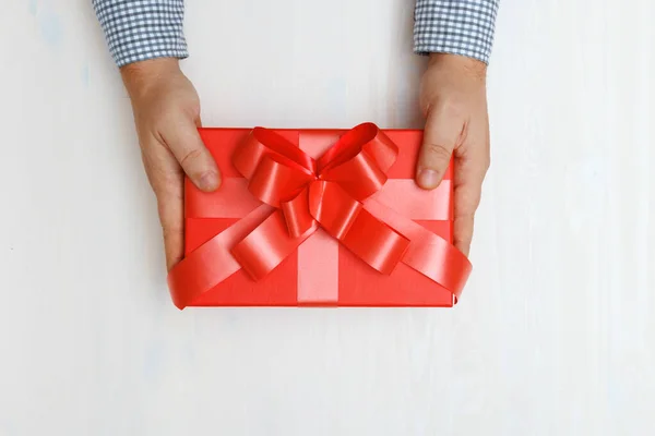 Nahaufnahme der Hand eines Mannes, der eine rote Schachtel mit einem Geschenk am Tisch überreicht. Ansicht von oben. Konzept des Valentinstages und der Weihnachtsfeier — Stockfoto