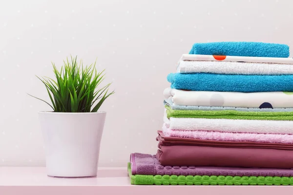Sur la commode, il y a une pile de linge de lit repassé propre, des serviettes pliées multicolores et une plante à la maison. — Photo